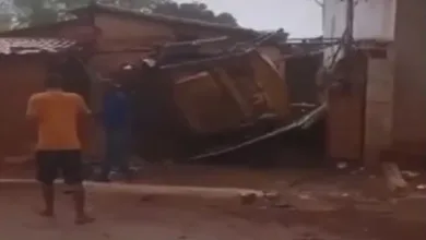 Trator transportado em caminhão cai de carroceria e atinge casa